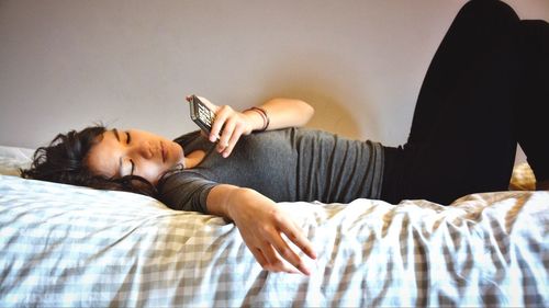 Woman using phone while lying on bed