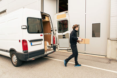 Male worker with box walking against delivery van on road towards entrance