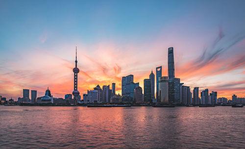 Modern buildings and river against sky during sunset