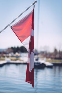 Close-up of canadian flag by lake on sunny day