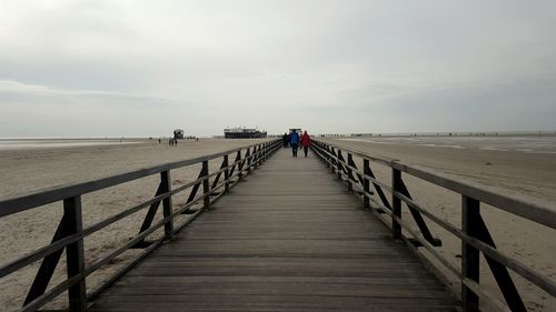 People walking on pier at beach against sky