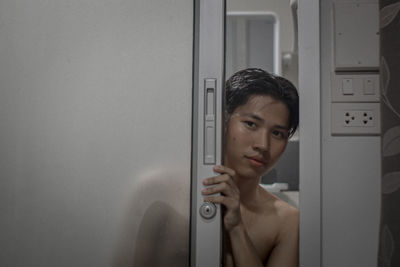 Portrait of shirtless young man looking through door