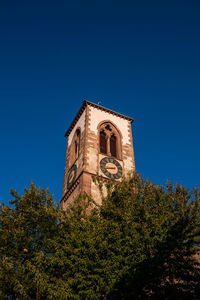 Low angle view of trees and building against clear blue sky