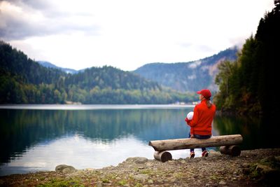 Rear view of two people sitting on bench in front of lake