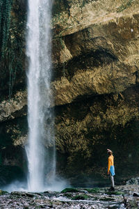 A young active woman in a yellow longsleeve near a large mountain waterfall.