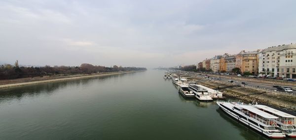 Boats moored in river by buildings in city against sky