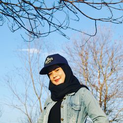 Portrait of smiling woman standing by bare tree against sky