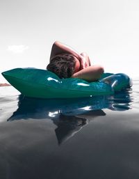 Young woman lying on inflatable raft in sea against sky