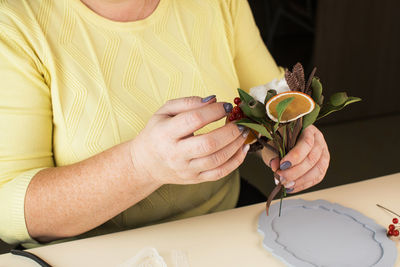 Woman holds small bouquet with cotton flowers and dry orange slices above table