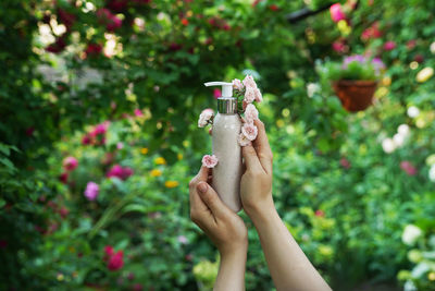 Cosmetic bottle with flowers in female hands on nature background 