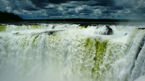 Scenic view of waterfall against cloudy sky