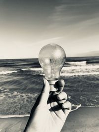 Close-up of hand holding crystal ball against sea