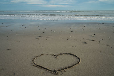 Heart shape on sand at beach against sky