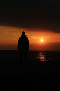 Rear view of silhouette man standing on beach at sunset