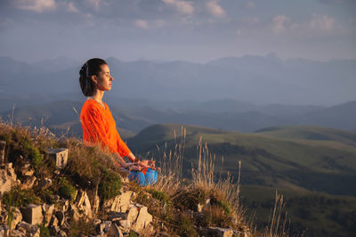 Meditating woman with closed eyes in bright clothes in the mountains, sportswear advertising banner