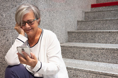 Smiling senior woman using mobile phone while sitting on staircase
