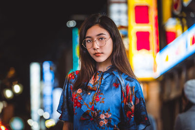 Portrait of young woman standing against illuminated wall