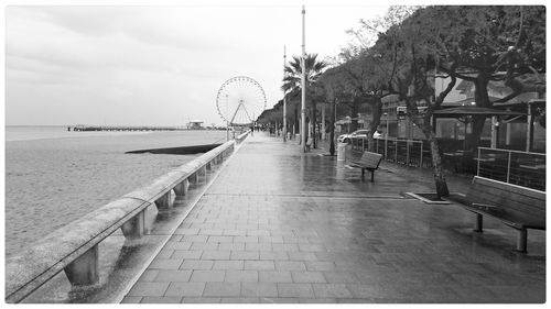 Promenade by sea by ferris wheel against sky