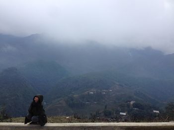 Woman sitting on retaining wall against mountain range