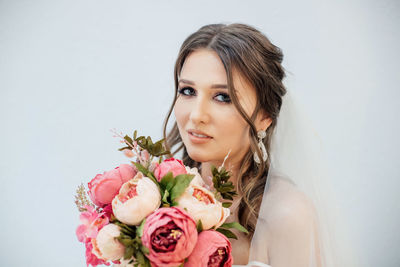 Portrait of woman with rose bouquet against white wall