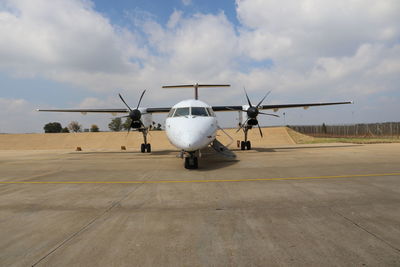 Airplane on airport runway against cloudy sky