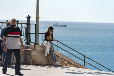 Men standing on railing by sea against sky