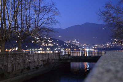 Illuminated buildings by river against sky at night