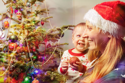 Portrait of smiling woman standing by christmas tree at home