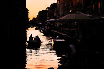 Silhouette people on boat in city at sunset