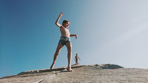 Low angle view of shirtless boy standing against clear sky