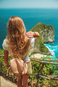 Travel girl with backpack in shorts on ocean and tropical beach background. nusa penida, indonesia