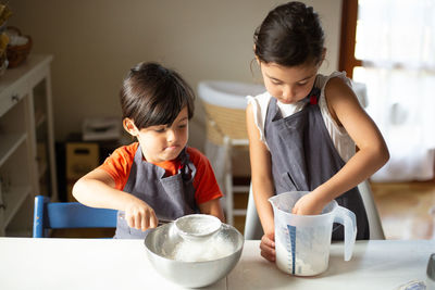 Two children wearing grey aprons sifting flour