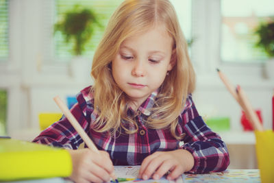 Girl drawing on book while sitting on table at home