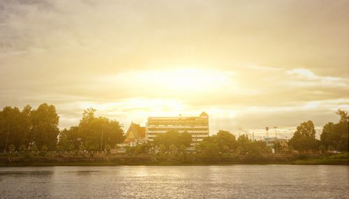 Scenic view of river by buildings against sky during sunset