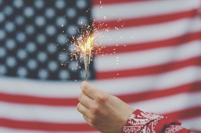 Cropped hand holding illuminated sparkler against american flag