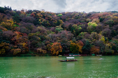 Boat sailing on river by trees against sky