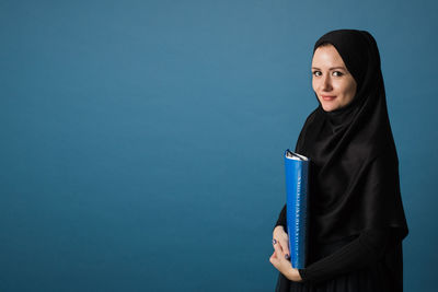 Portrait of smiling young woman standing against blue wall