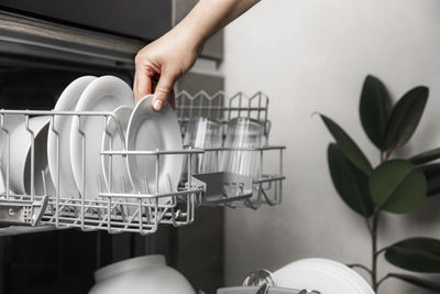 Close-up of female hand loading dished to, empty out or unloading from open dishwasher machine