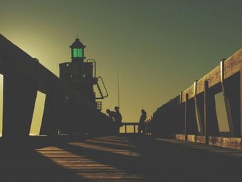 Silhouette people walking on footpath against clear sky