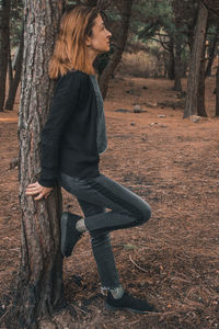 Side view of young woman with tree trunk in forest