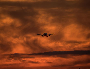 Silhouette airplane flying in orange sky