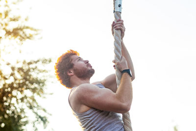 Low angle view of man holding rope against sky