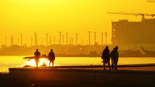 Silhouette people by sea against sky during sunset