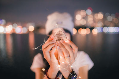 Midsection of woman holding illuminated lights against sky at night