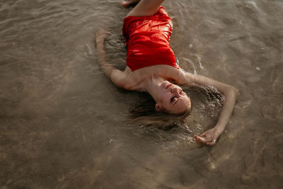 A young girl in a red dress lies in sea water