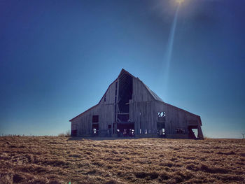 Barn on field against clear blue sky