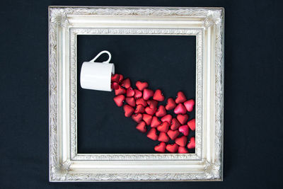 Directly above shot of red heart shapes and cup in picture frame on black background