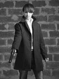 Young man holding gun against wall