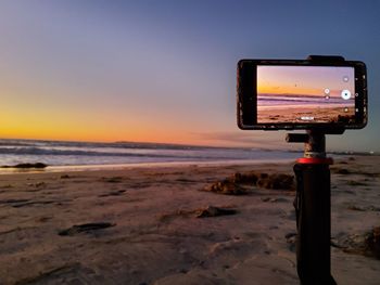 Mobile on tripod  on beach against sky during sunset