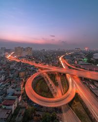 Aerial view of light trails on road amidst buildings against sky during sunset